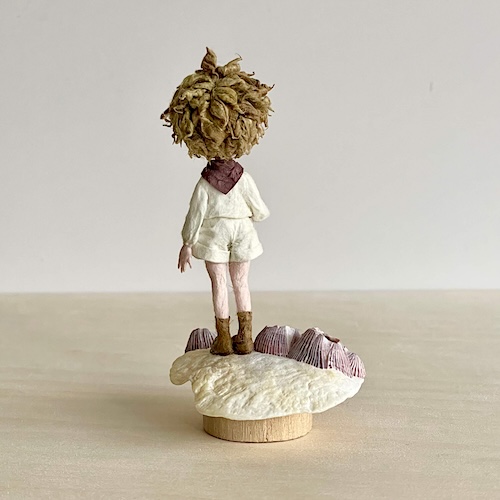 貝殻の上に佇む和紙人形の完成作品。静かな旅を思わせる物語性のある造形。(背面)