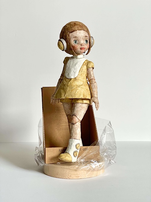 和紙人形「未来のかたち(ミライちゃん)」。クルミやザクロで染めたロクタ紙の質感と、耳の機械パーツが特徴で、未来的な存在と人形らしさが混ざったデザイン。