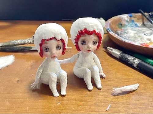 小さな双子のさくらんぼ人形に座りポーズを付けている様子。下向きの視線が特徴的な造形。