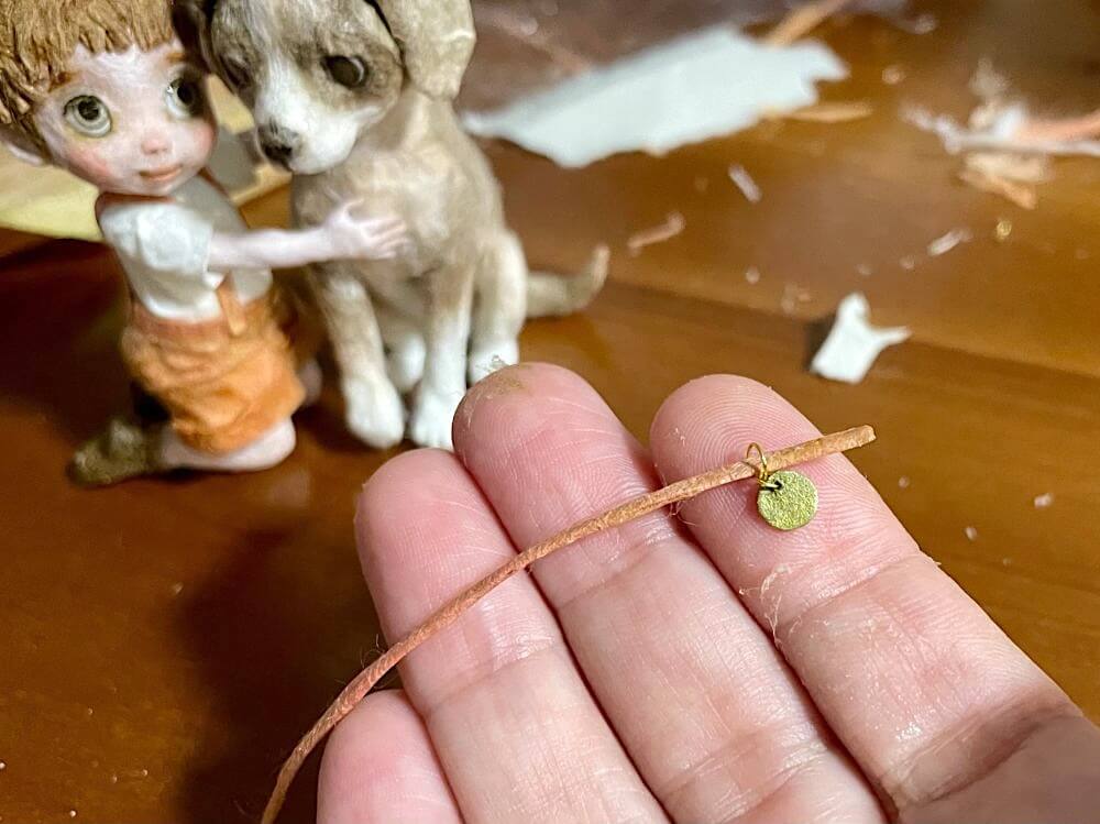 犬の首輪を製作中、金色のメダルが付いたデザイン。少年と犬の世界観を整えている細部制作の様子。
