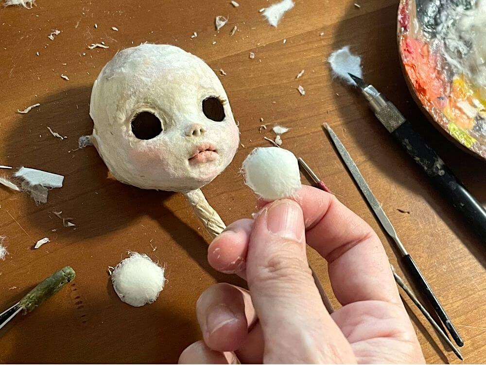 和紙人形の顔を作りながら、目のパーツを手に持っているところ